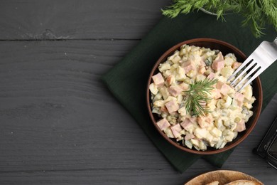 Photo of Tasty Olivier salad with boiled sausage in bowl served on grey wooden table, flat lay. Space for text