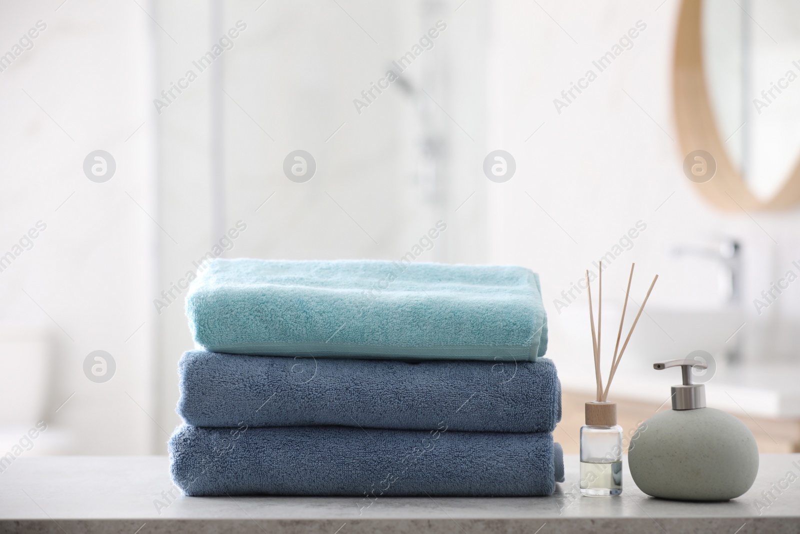 Photo of Stack of fresh towels, reed air freshener and soap dispenser on table in bathroom