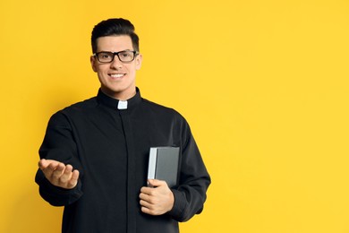 Priest in cassock with Bible on yellow background. Space for text