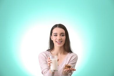 Photo of Beautiful young woman drinking milk with cookies on color background