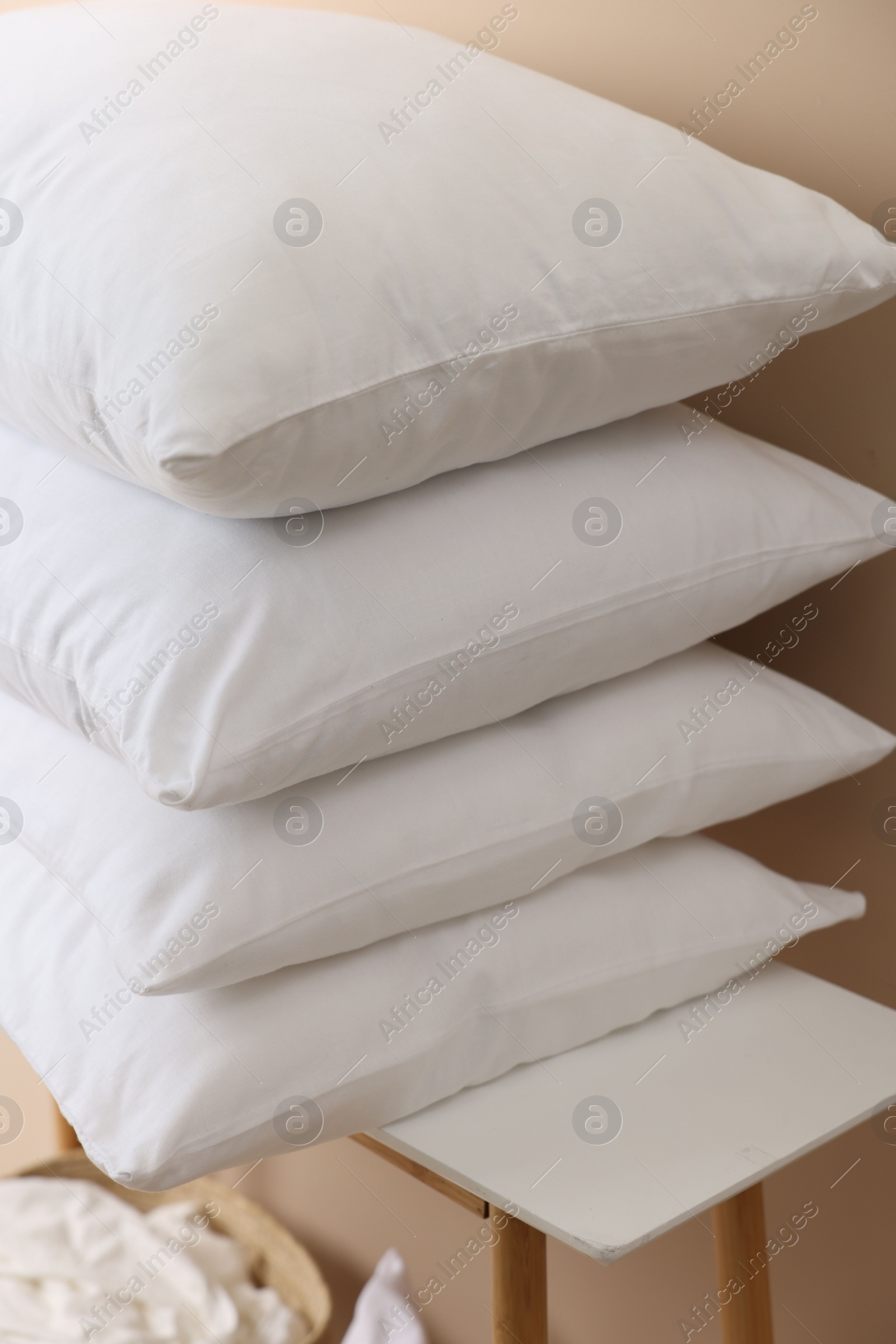 Photo of Stack of soft white pillows on table near beige wall