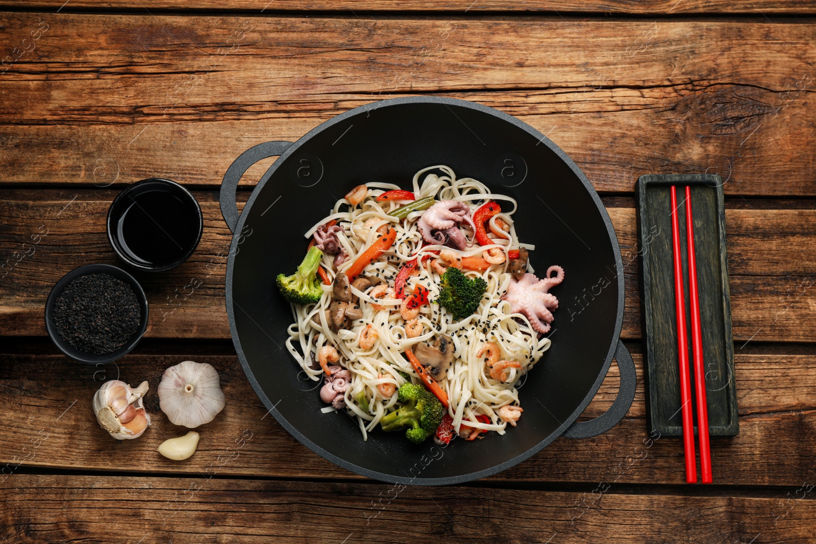 Photo of Stir fried noodles with seafood and vegetables in wok on wooden table, flat lay