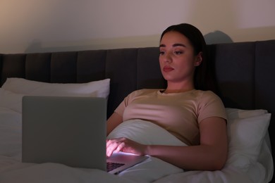 Photo of Young woman using laptop in bed at night. Internet addiction