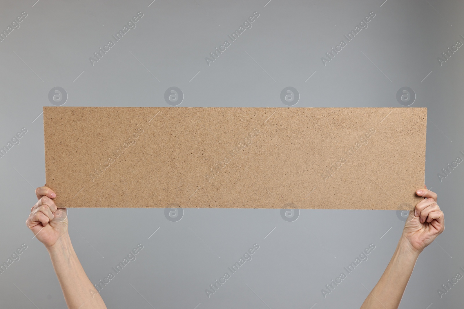 Photo of Woman holding blank cardboard banner on grey background, closeup. Space for text