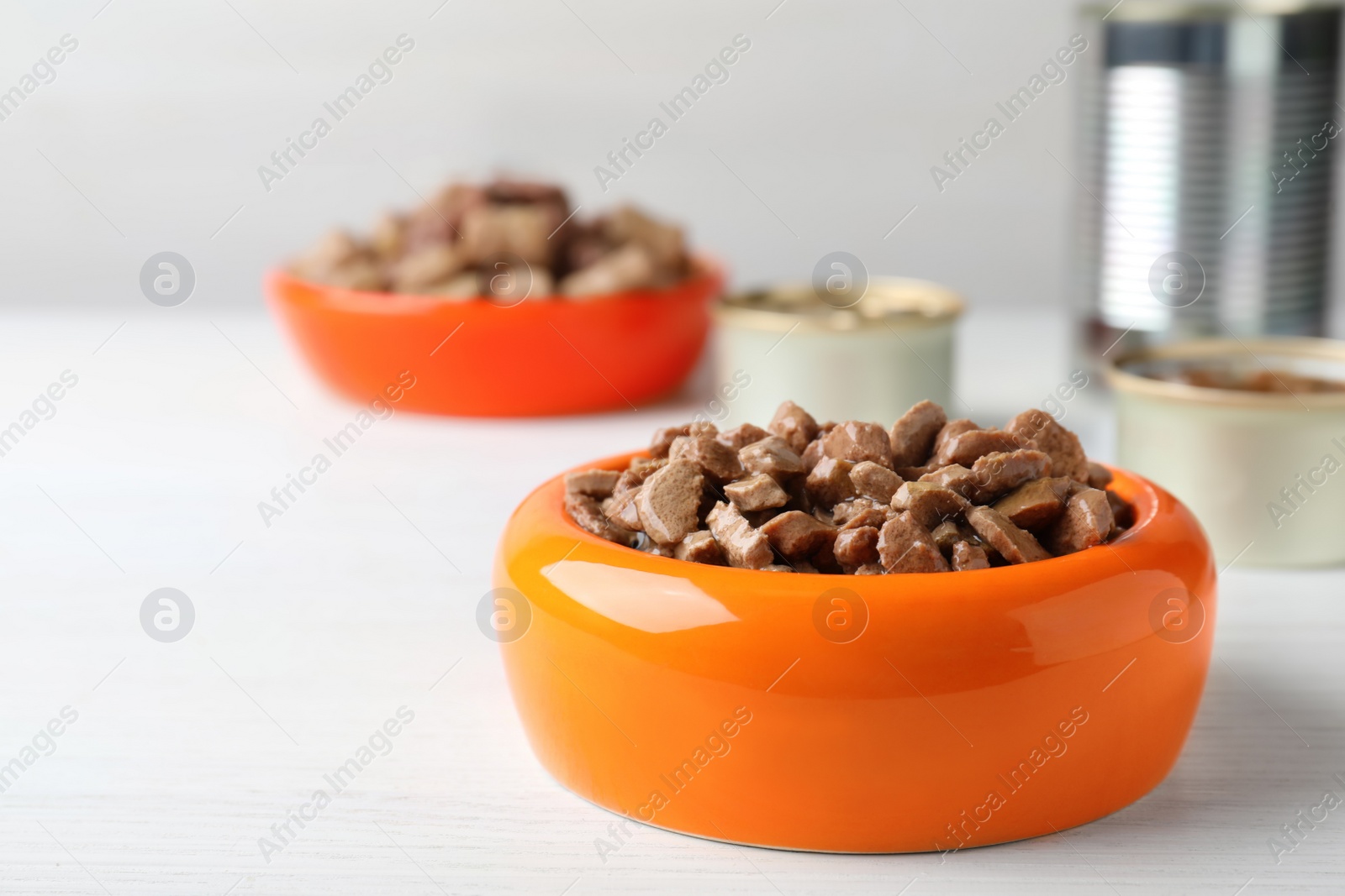 Photo of Wet pet food in feeding bowl on white wooden table. Space for text