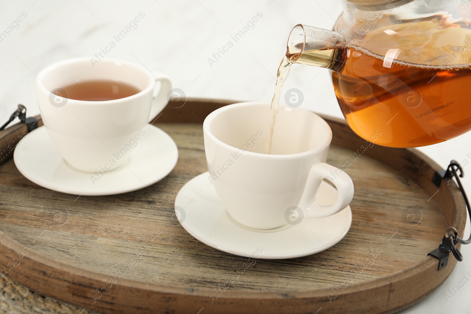 Photo of Pouring aromatic tea in cup at table, closeup