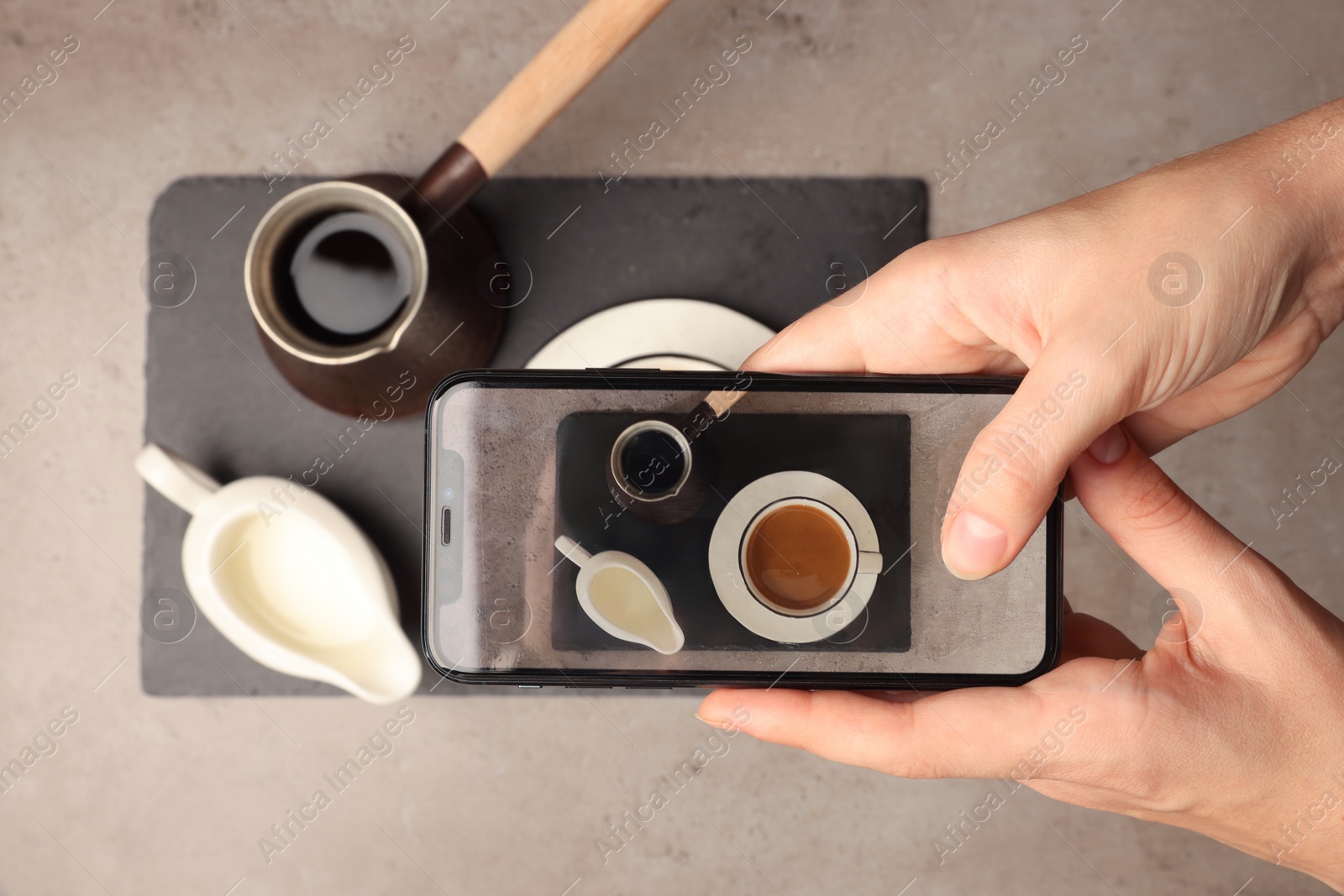 Photo of Woman taking photo of Turkish coffee and milk with smartphone at grey table, top view