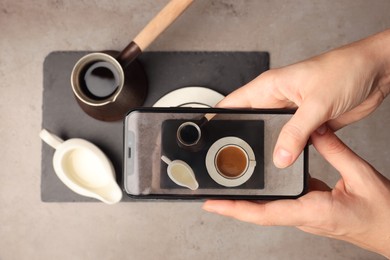 Photo of Woman taking photo of Turkish coffee and milk with smartphone at grey table, top view