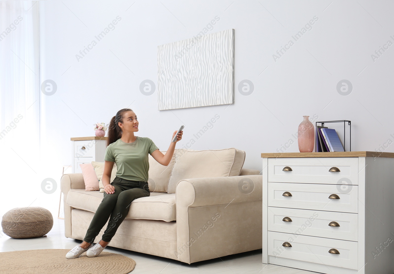 Photo of Happy young woman switching on air conditioner with remote control at home