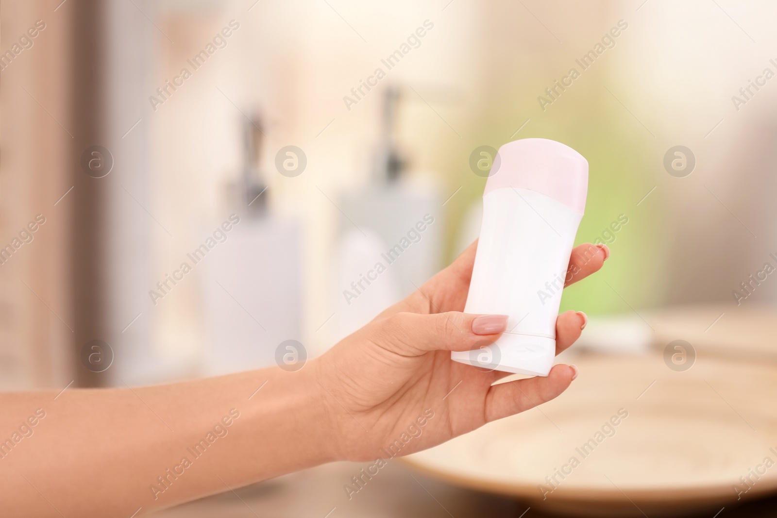 Photo of Young woman holding deodorant in bathroom, closeup