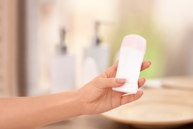 Photo of Young woman holding deodorant in bathroom, closeup