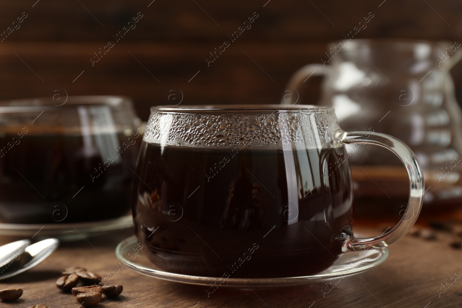 Photo of Hot coffee in glass cups and beans on wooden table, closeup