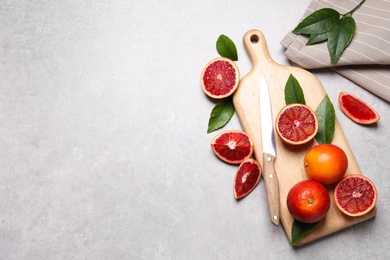 Photo of Ripe red oranges, green leaves and wooden board with knife on light table, flat lay. Space for text