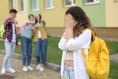 Photo of Teen problems. Group of students pointing at upset girl outdoors, selective focus