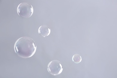 Photo of Beautiful translucent soap bubbles on grey background. Space for text