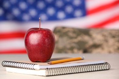 Photo of Notebooks, apple and pencil on light table against flag of USA. Military education