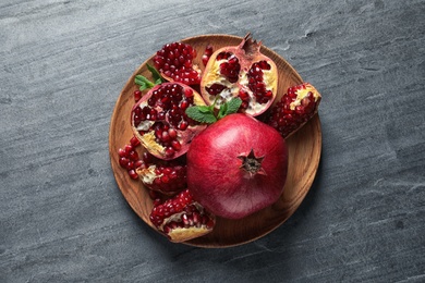 Photo of Plate with ripe pomegranates on grey background, top view