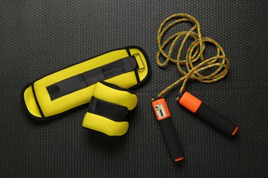 Photo of Yellow weighting agents and skipping rope on yoga mat, flat lay
