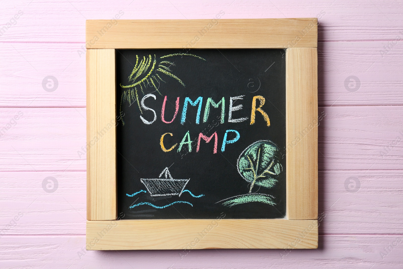 Photo of Chalkboard with text SUMMER CAMP and drawings on wooden background, top view