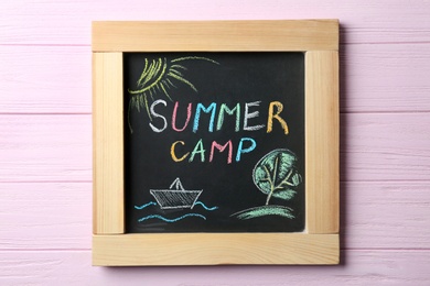 Photo of Chalkboard with text SUMMER CAMP and drawings on wooden background, top view