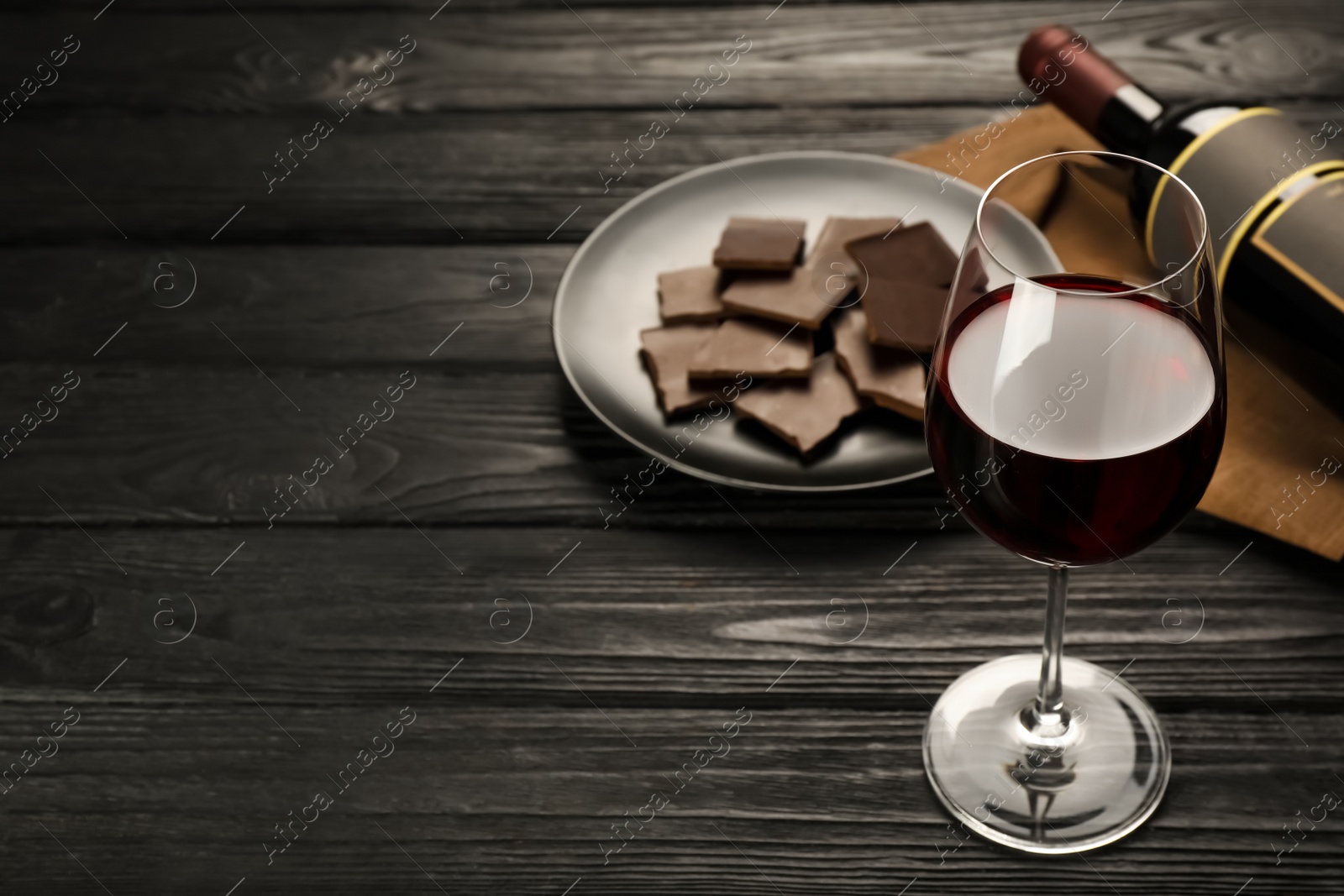 Photo of Tasty red wine and chocolate on black wooden table. Space for text