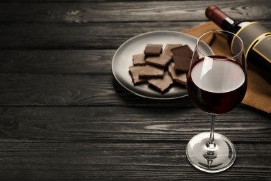 Photo of Tasty red wine and chocolate on black wooden table. Space for text