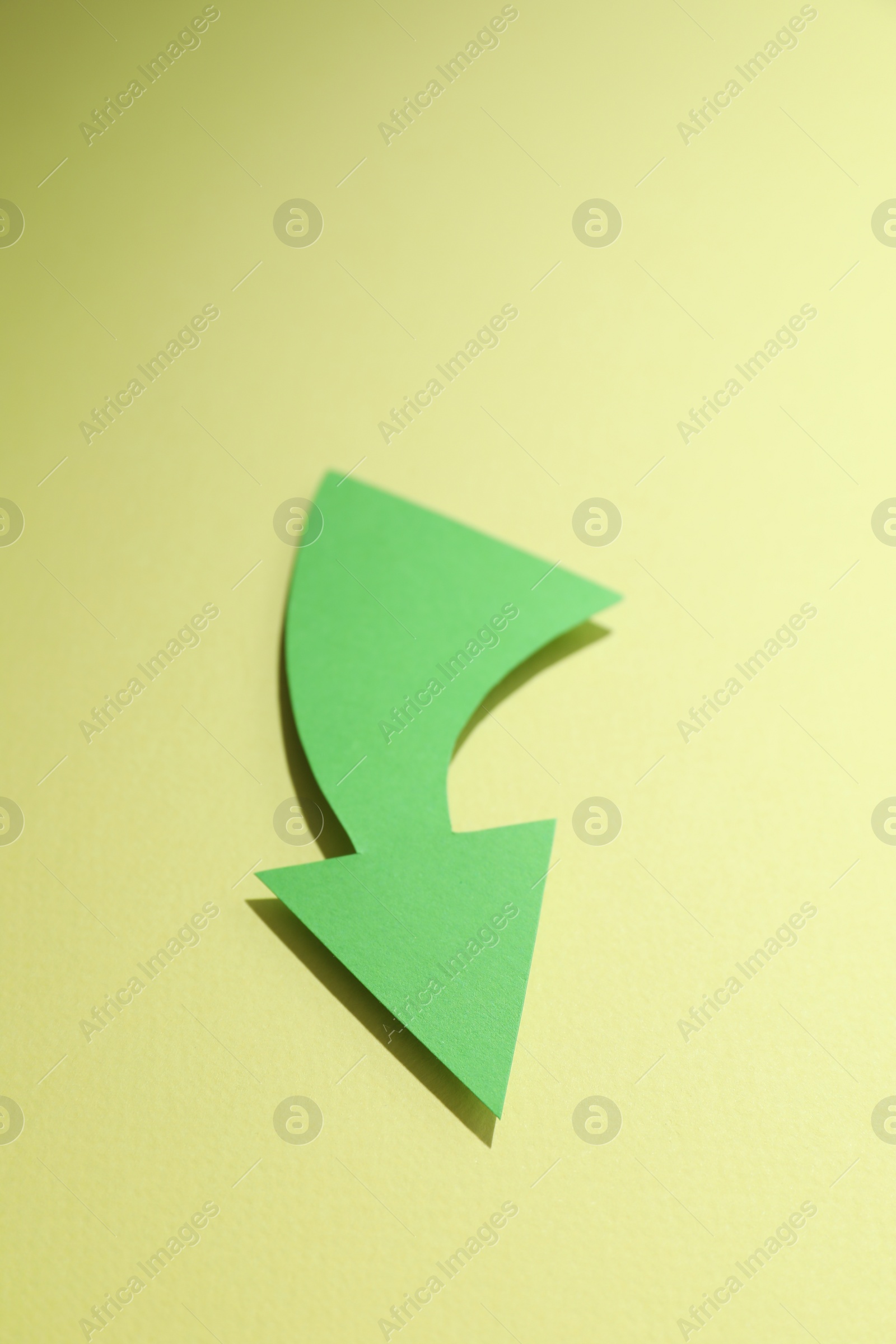 Photo of Curved green paper arrow on yellow background