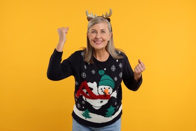 Photo of Happy senior woman in Christmas sweater and deer headband on orange background