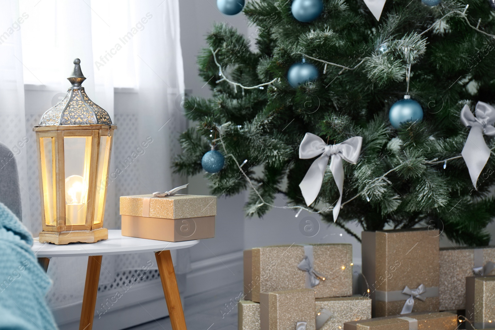 Photo of Decorative lantern on table and Christmas tree with gift boxes in stylish living room interior