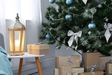 Decorative lantern on table and Christmas tree with gift boxes in stylish living room interior