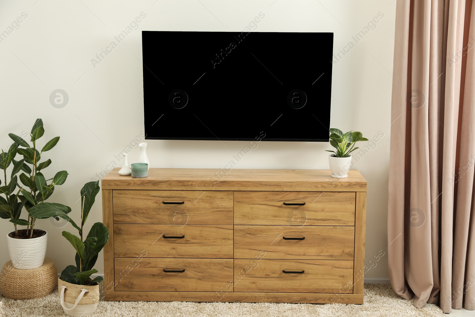 Photo of Cozy room interior with chest of drawers, TV set and decor elements