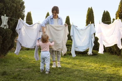 Mother and daughter hanging clothes with clothespins on washing line for drying in backyard, back view