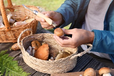 Photo of Man cleaning mushroom with brush on knife at table outdoors, closeup