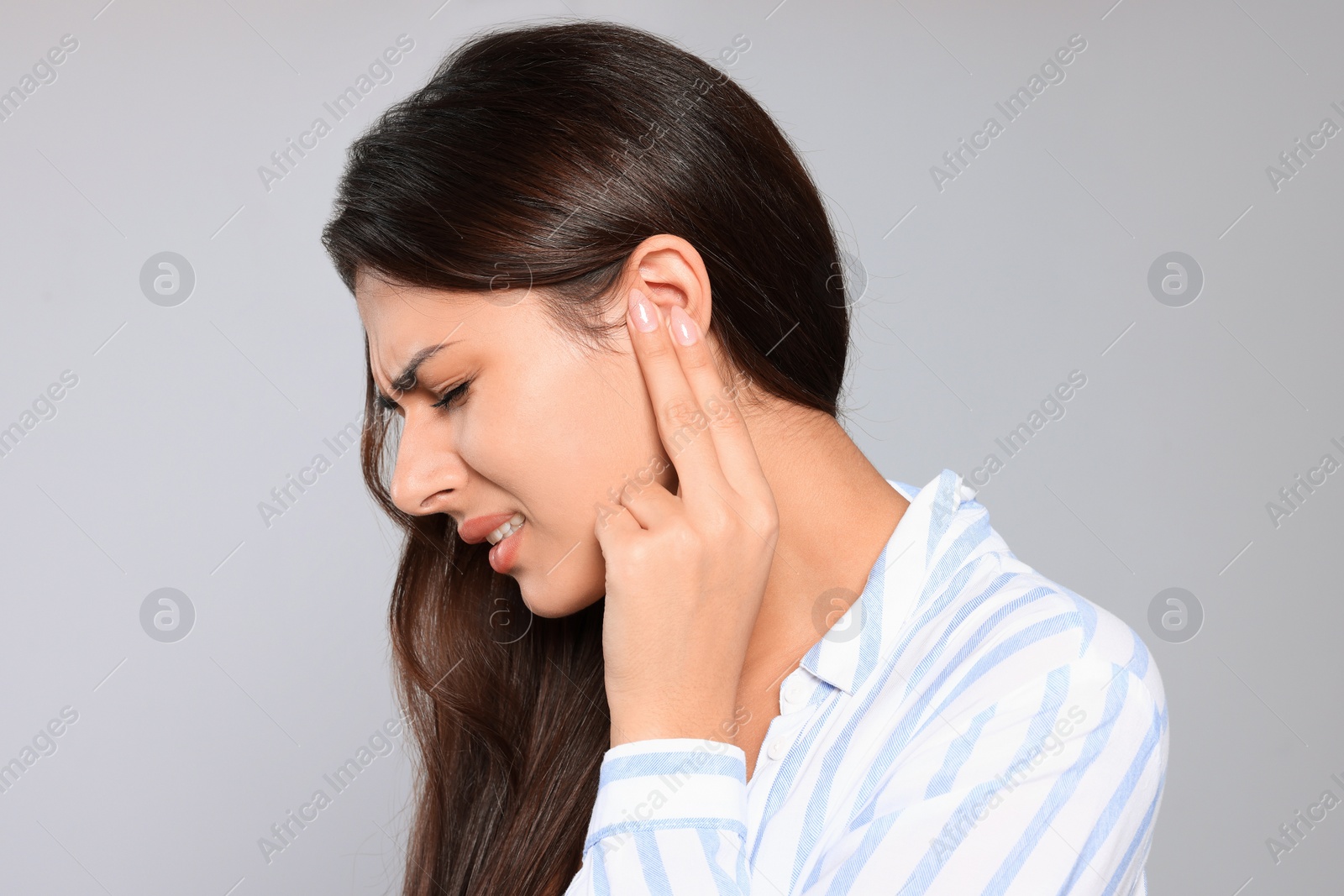 Photo of Young woman suffering from ear pain on light grey background