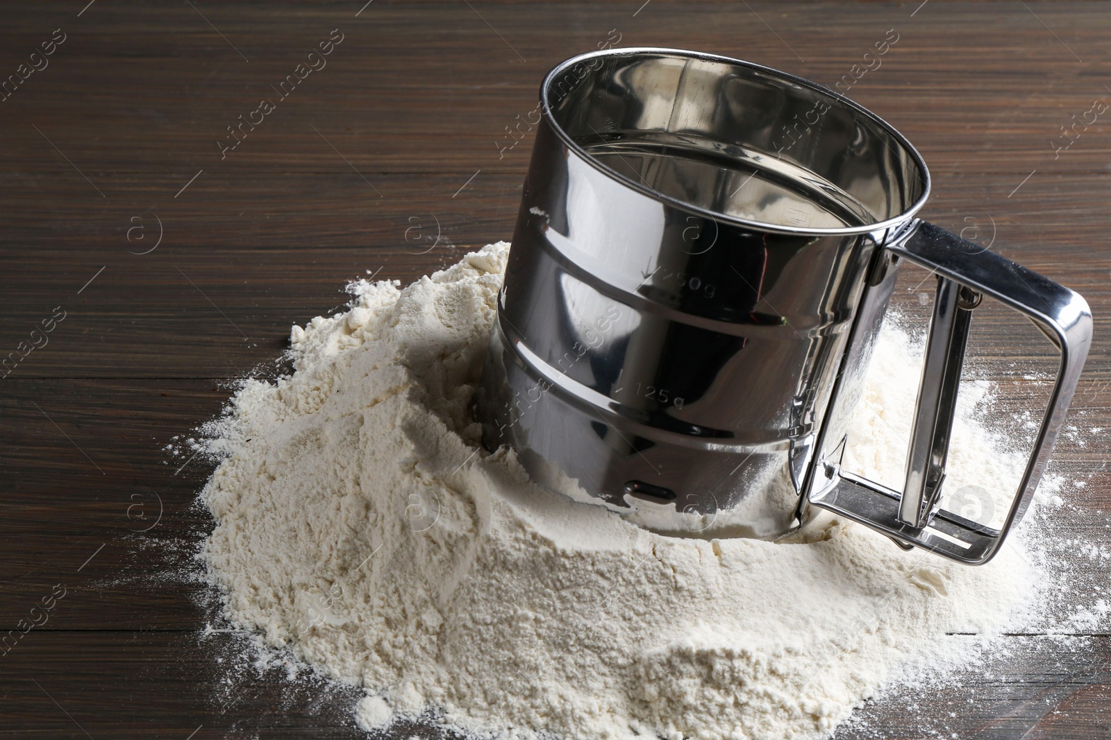 Photo of Sifter and pile of flour on wooden table, closeup