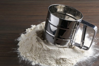 Photo of Sifter and pile of flour on wooden table, closeup