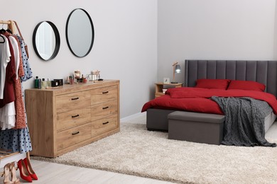Stylish bedroom with comfortable bed and wooden chest of drawers. Interior design