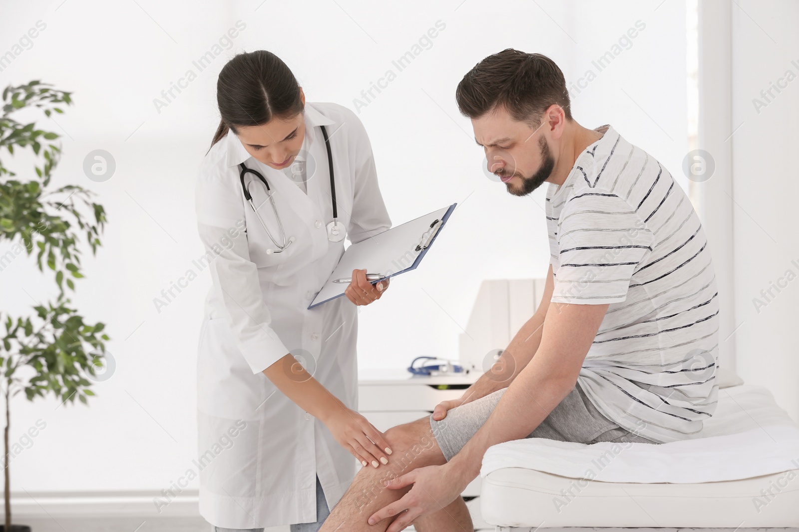 Photo of Doctor examining male patient with injured leg in clinic