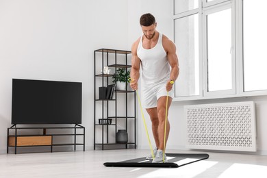 Photo of Muscular man doing exercise with elastic resistance band on mat at home