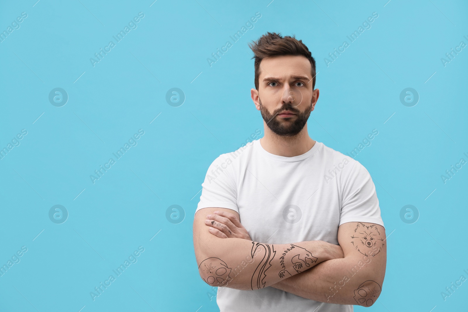 Image of Handsome man with beautiful tattoo sketches on light blue background. Space for text