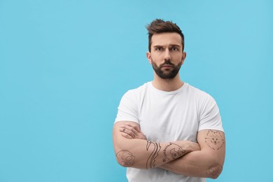 Image of Handsome man with beautiful tattoo sketches on light blue background. Space for text