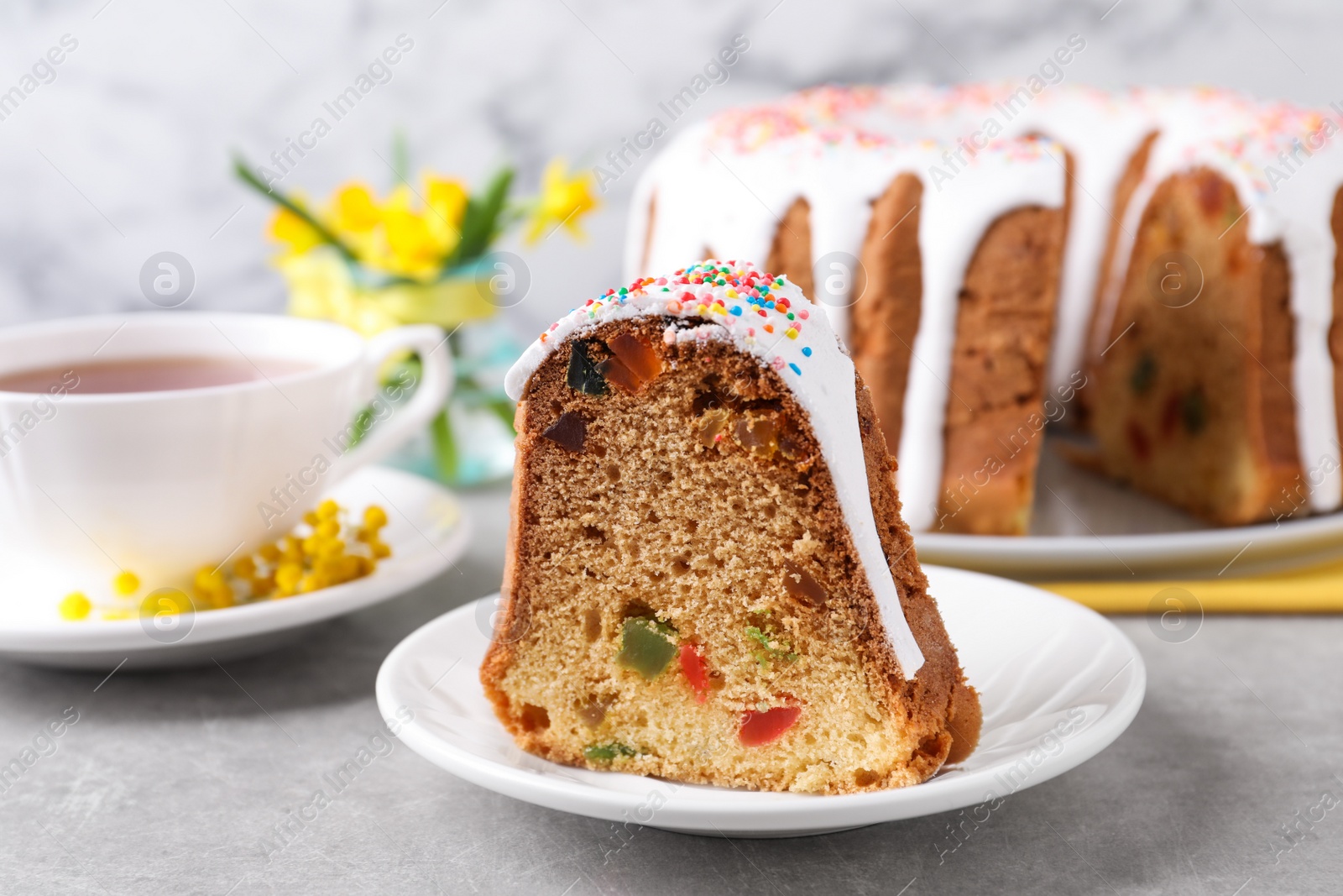 Photo of Piece of glazed Easter cake with sprinkles and candied fruits on grey table, closeup