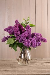 Photo of Beautiful lilac flowers in vase on wooden table