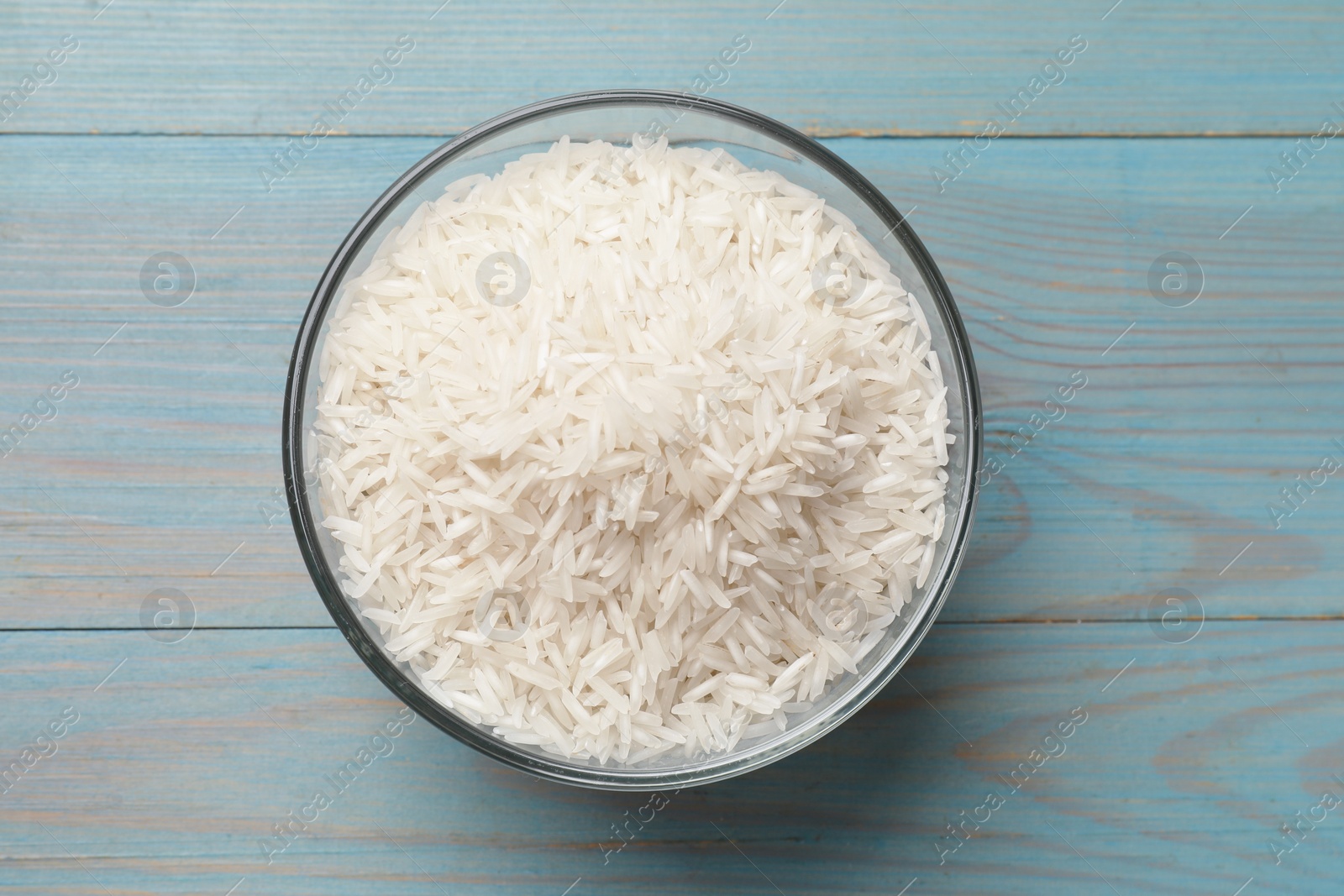 Photo of Raw basmati rice in bowl on light blue wooden table, top view