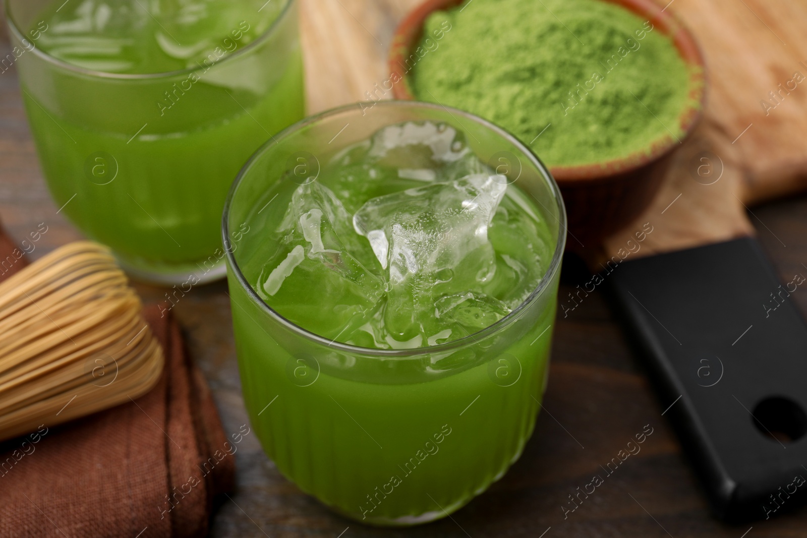 Photo of Delicious iced green matcha tea, powder and bamboo whisk on wooden table, closeup