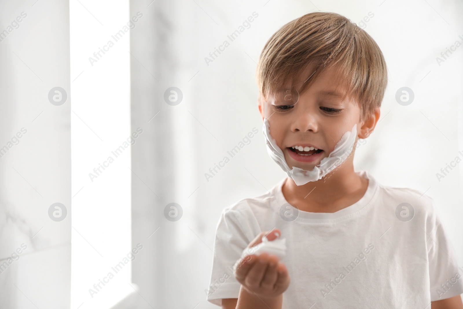 Photo of Little boy with shaving foam on face indoors. Space for text