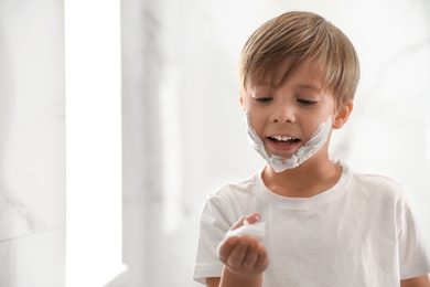 Photo of Little boy with shaving foam on face indoors. Space for text