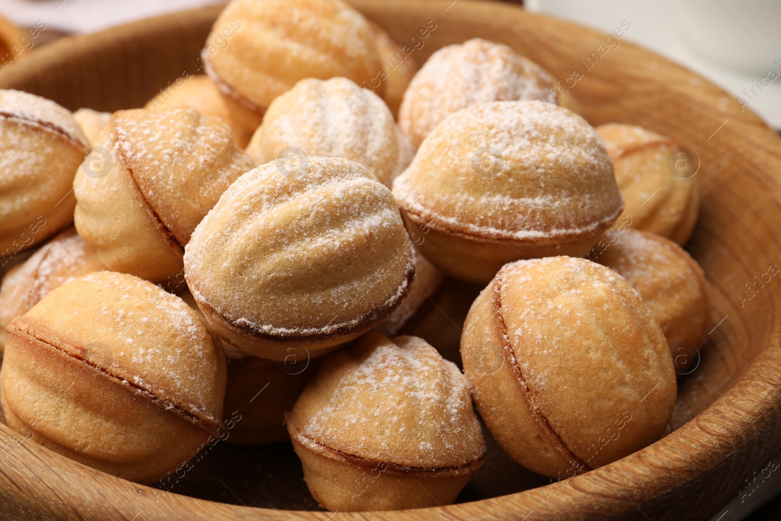 Photo of Delicious nut shaped cookies with boiled condensed milk and powdered sugar on wooden table, closeup