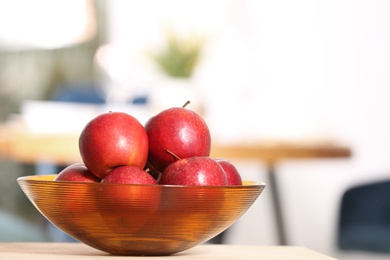 Photo of Bowl with sweet red apples on table in room, space for text