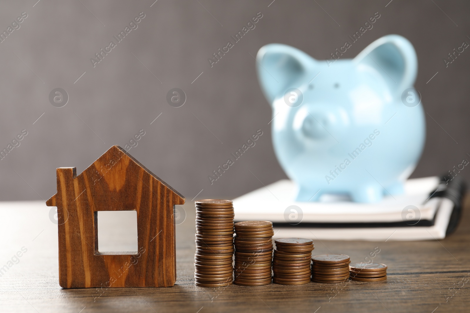 Photo of House model, stacked coins, piggy bank and notebook on wooden table, selective focus